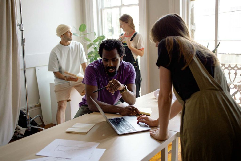 Creative team working together around a laptop in a bright studio, About Us at BURG+CO. Marketing
